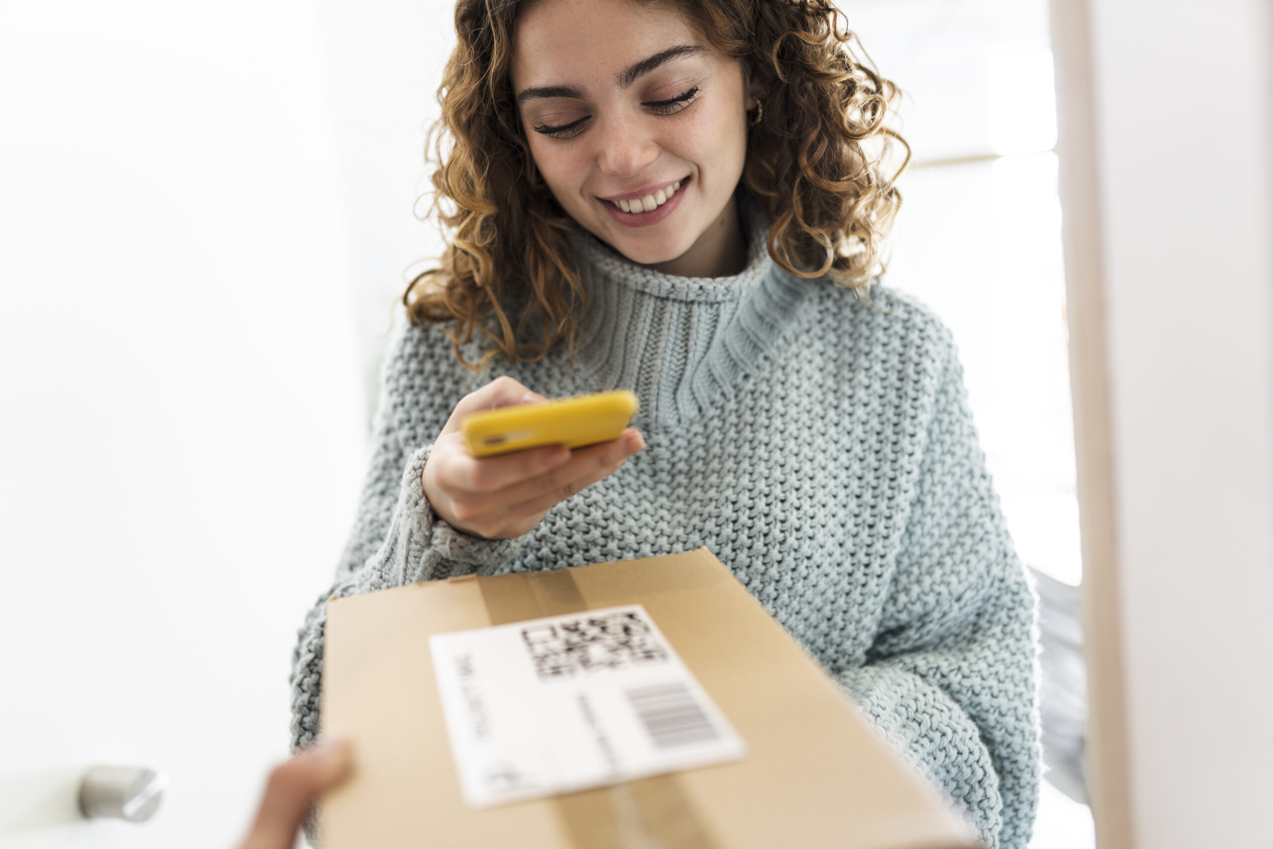 Woman scanning QR code on package that is being delivered on her doorstep