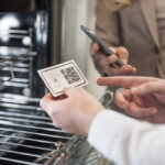 A man showing his business card with a QR code to a customer in front of an oven.