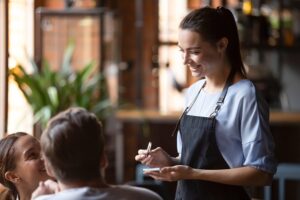 An image of a server taking an order from two guests in a restaurant.