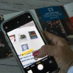 A woman holding a phone, trying to scan a small QR code from a brochure. A woman scans a QR code from a brochure to open the webshop.