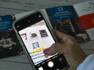 A woman holding a phone, trying to scan a small QR code from a brochure. A woman scans a QR code from a brochure to open the webshop.